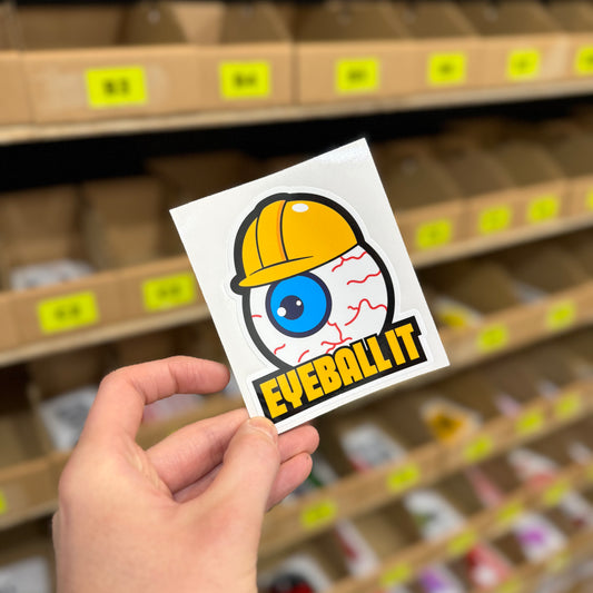 Eyeball It funny vinyl car sticker featuring cartoon eyeball wearing yellow hard hat, photographed in Blum Decals fulfilment area. Trades humour decal printed on waterproof gloss laminated vinyl, UK made.