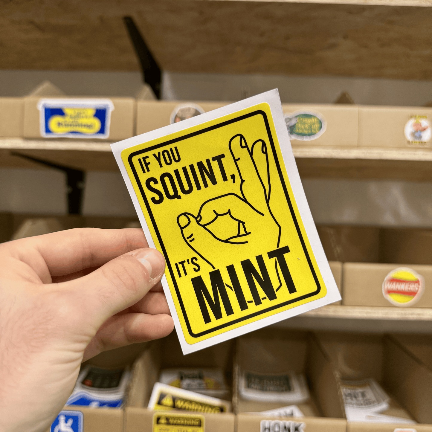 Bold yellow sticker with a simple line drawing hand gesture and the text ‘If you squint, it’s mint.’