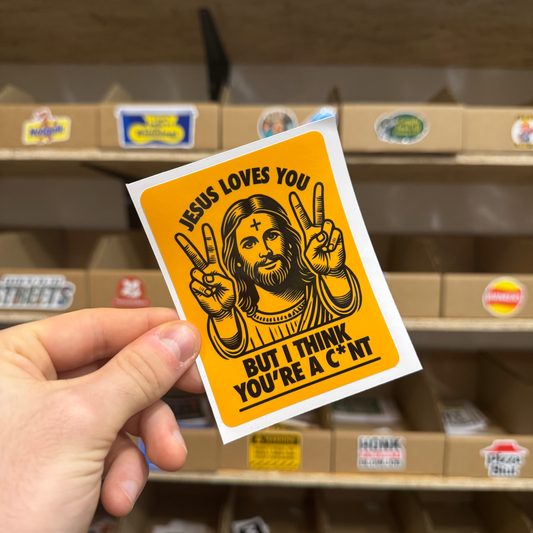 Bold orange sticker showing a cartoon Jesus holding up peace signs with the text ‘Jesus loves you but I think you’re a c*nt.’