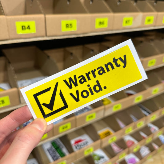 Yellow “Warranty void” warning style funny vinyl sticker held in hand.