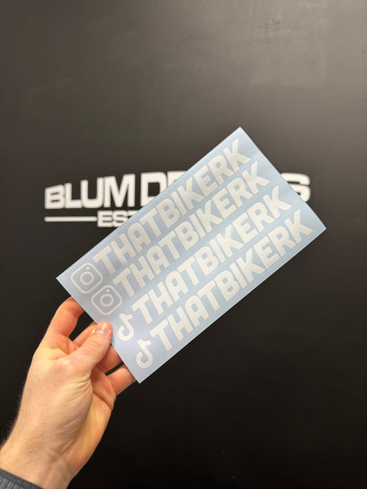 Gloss white vinyl stickers with a username text accompanied by Instagram and TikTok logos. The background features a black wall with partially visible white text reading "BLUM DECALS".