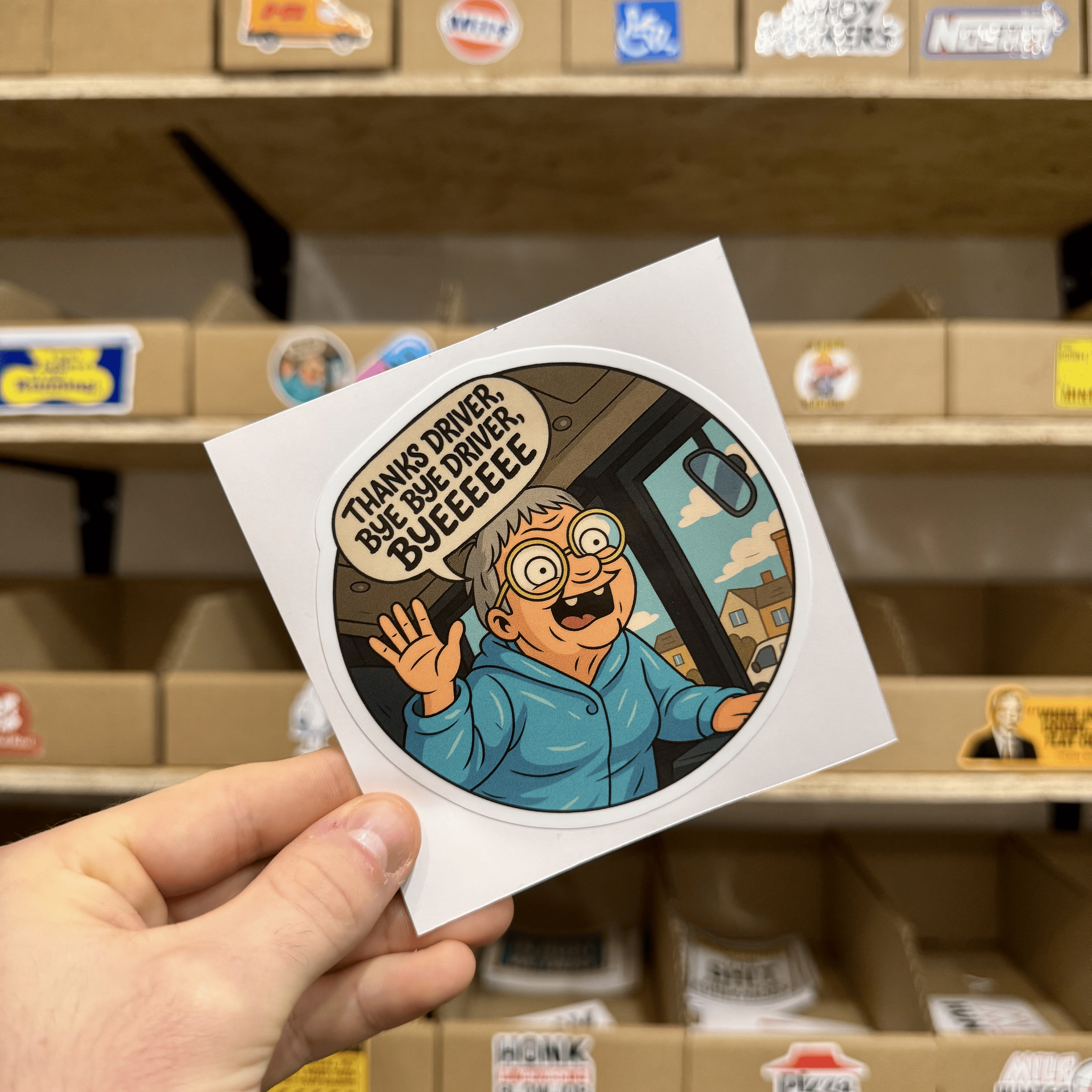 Cartoon-style round sticker showing an excited elderly person waving from the doorway of a bus, saying ‘Thanks driver, bye bye driver, byeeeee.’