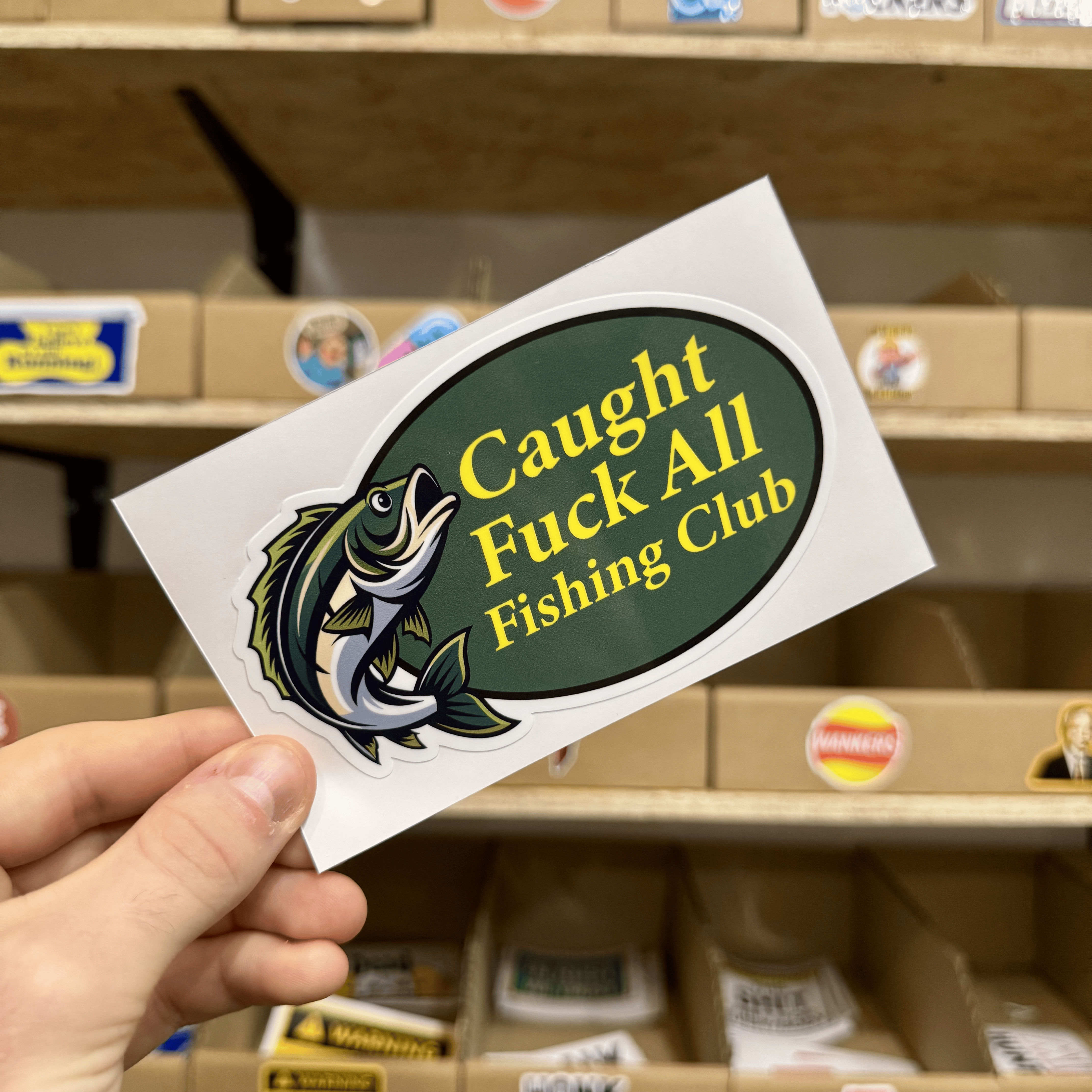 Green oval sticker with a jumping fish illustration and the humorous text ‘Caught Fuck All Fishing Club.’