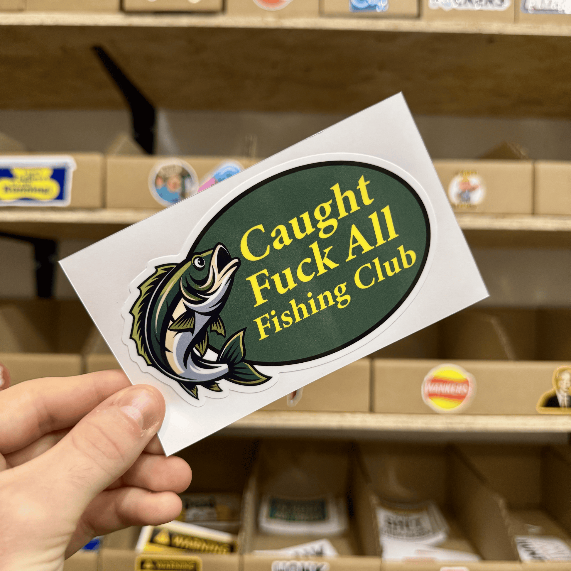 Green oval sticker with a jumping fish illustration and the humorous text ‘Caught Fuck All Fishing Club.’