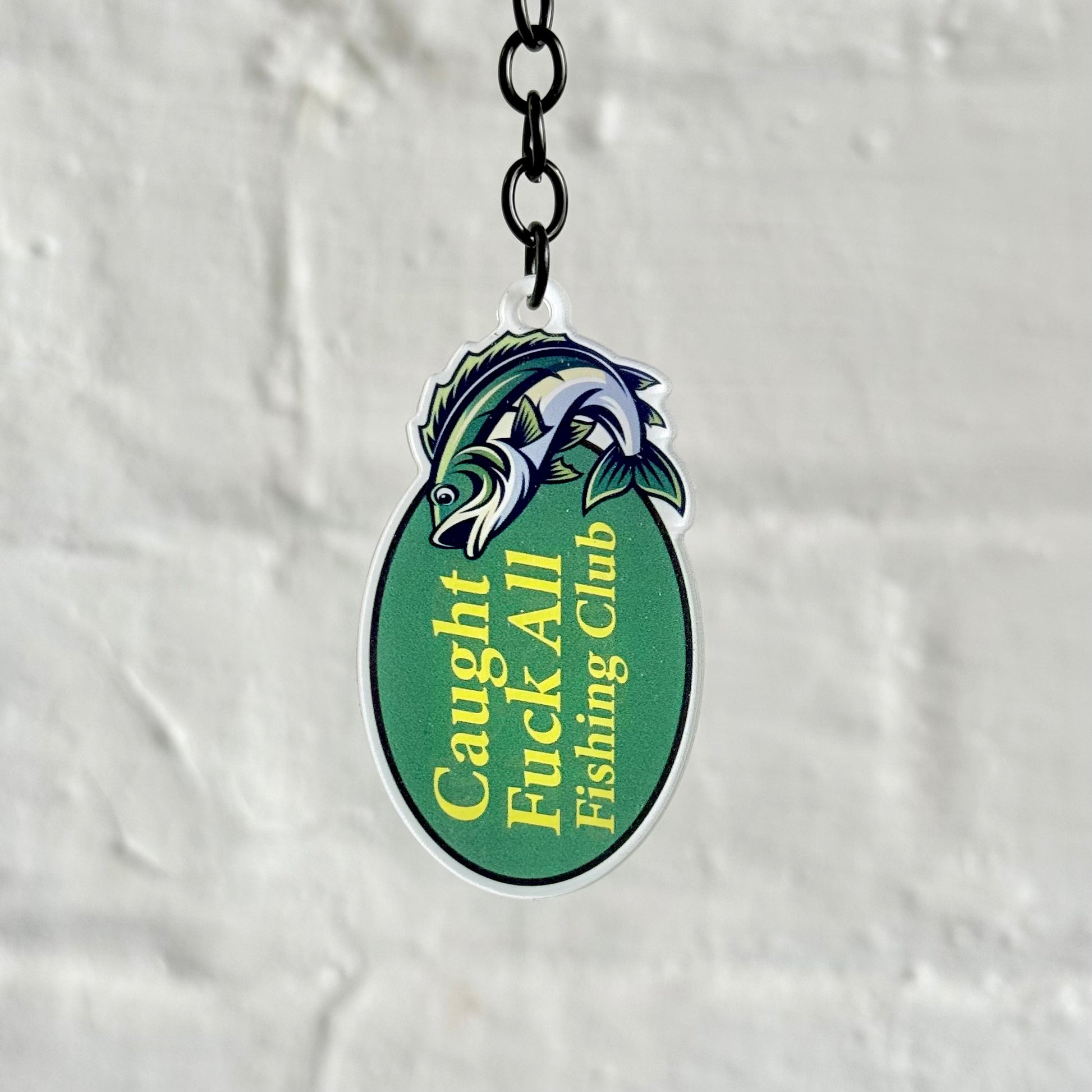 Funny “Caught F*ck All Fishing Club” acrylic keychain with green oval fish design, glossy finish and black chain, ideal novelty gift for anglers.