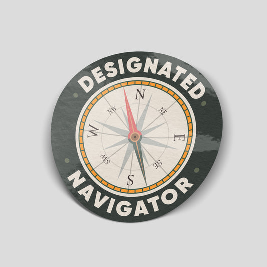 Round dark green Designated Navigator sticker with cream lettering and a vintage-style compass with a red needle and orange details.