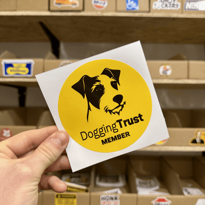 Yellow circular sticker with a black illustration of a dog’s face and the text ‘Dogging Trust Member.’