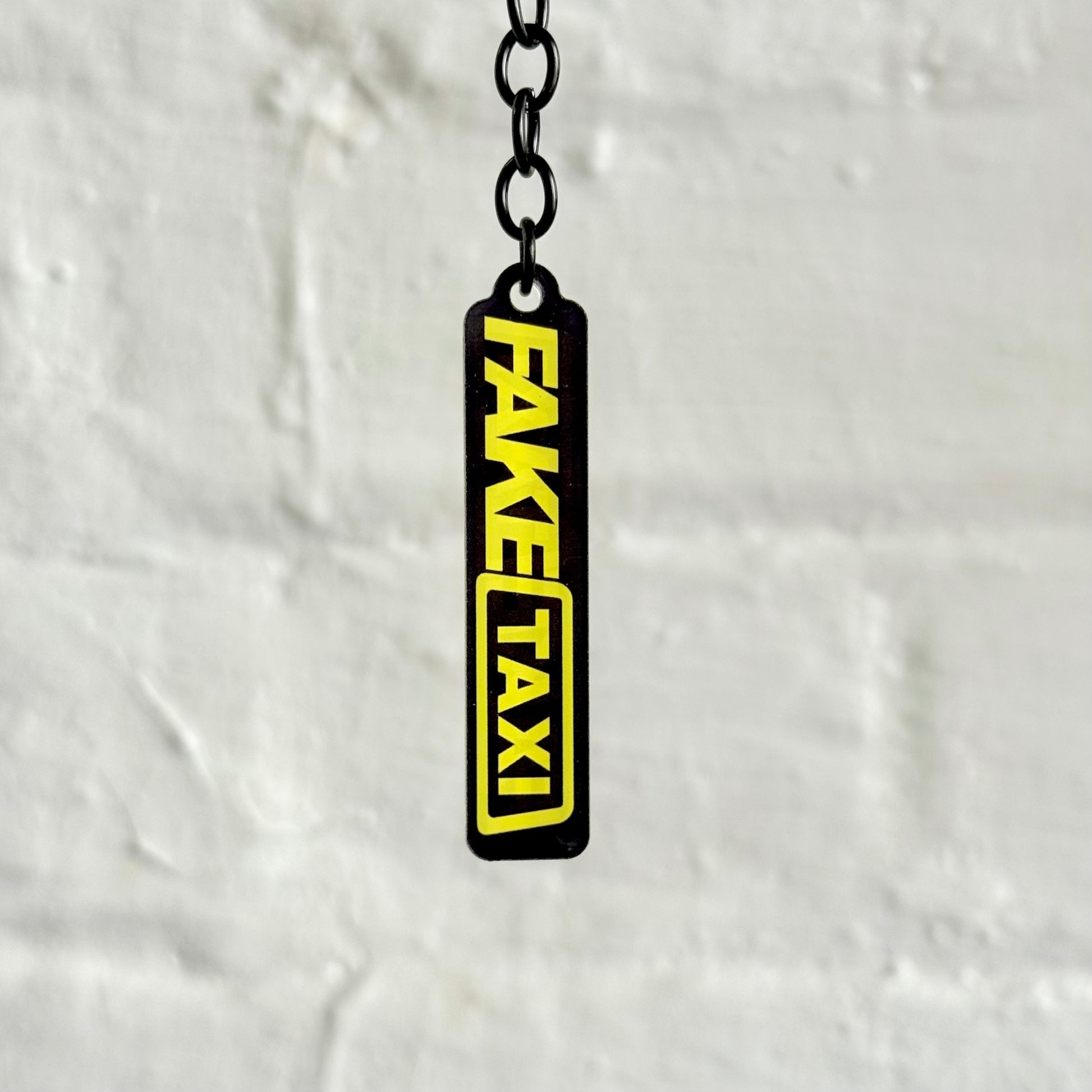 Funny “Fake Taxi” acrylic keychain with bold black and yellow design, glossy finish and black chain, novelty car keyring for automotive humour fans.
