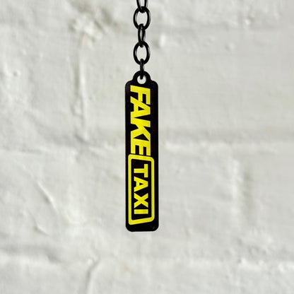 Funny “Fake Taxi” acrylic keychain with bold black and yellow design, glossy finish and black chain, novelty car keyring for automotive humour fans.