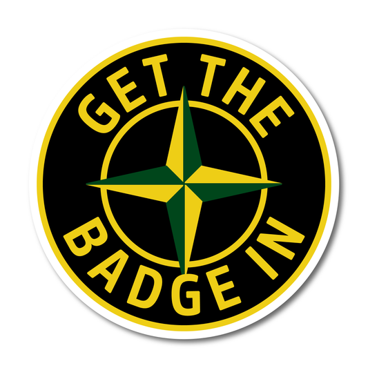 A round black sticker with a green and yellow compass-style star in the centre and the phrase “Get The Badge In” in bold yellow lettering.