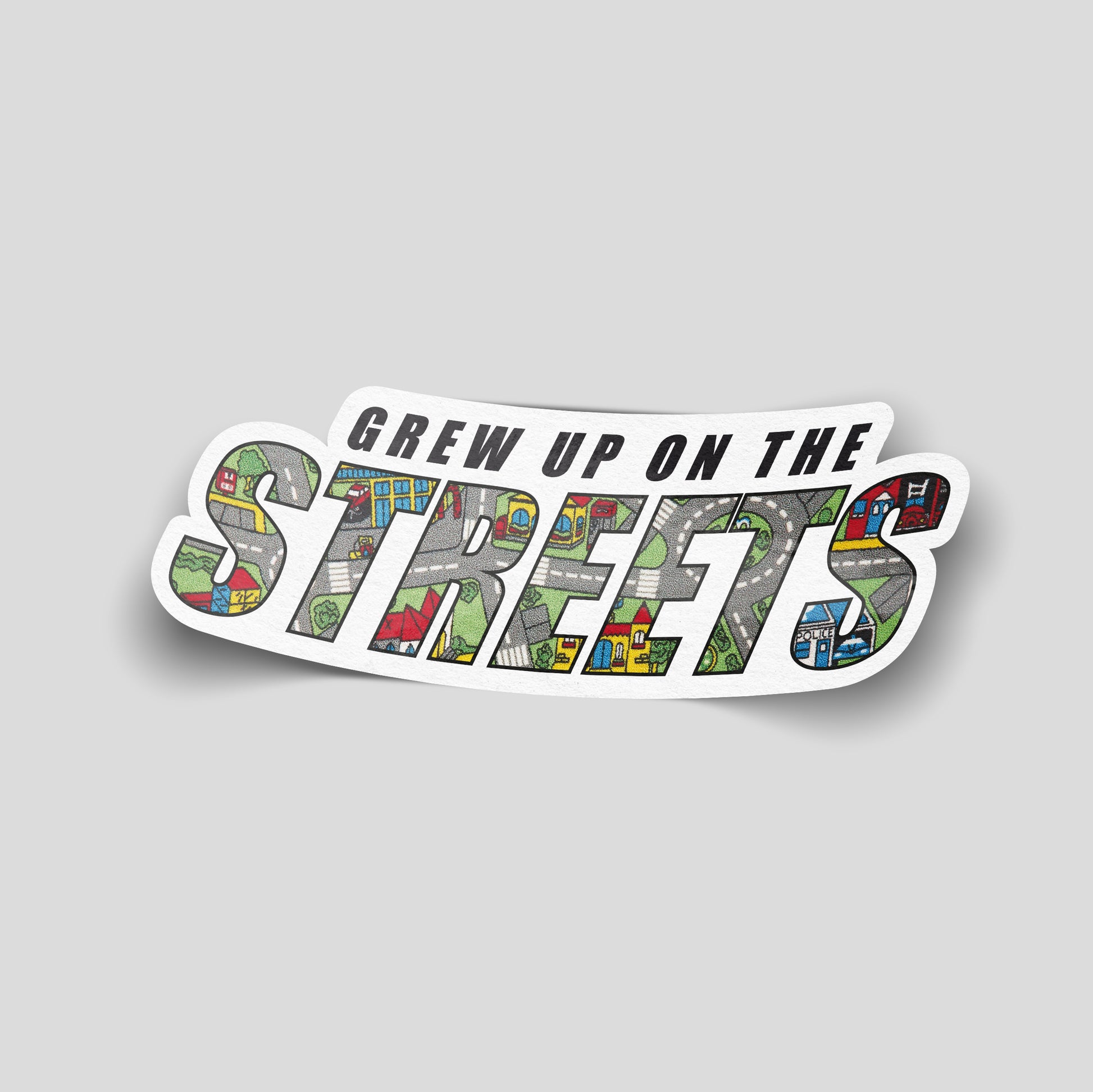 “Grew Up on the Streets” funny car sticker with text filled by a children’s play‑mat road pattern, UK nostalgia humour decal.