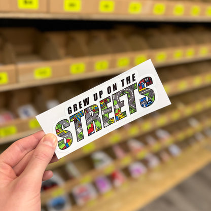Funny childhood parody sticker reading “grew up on the streets” with road map design