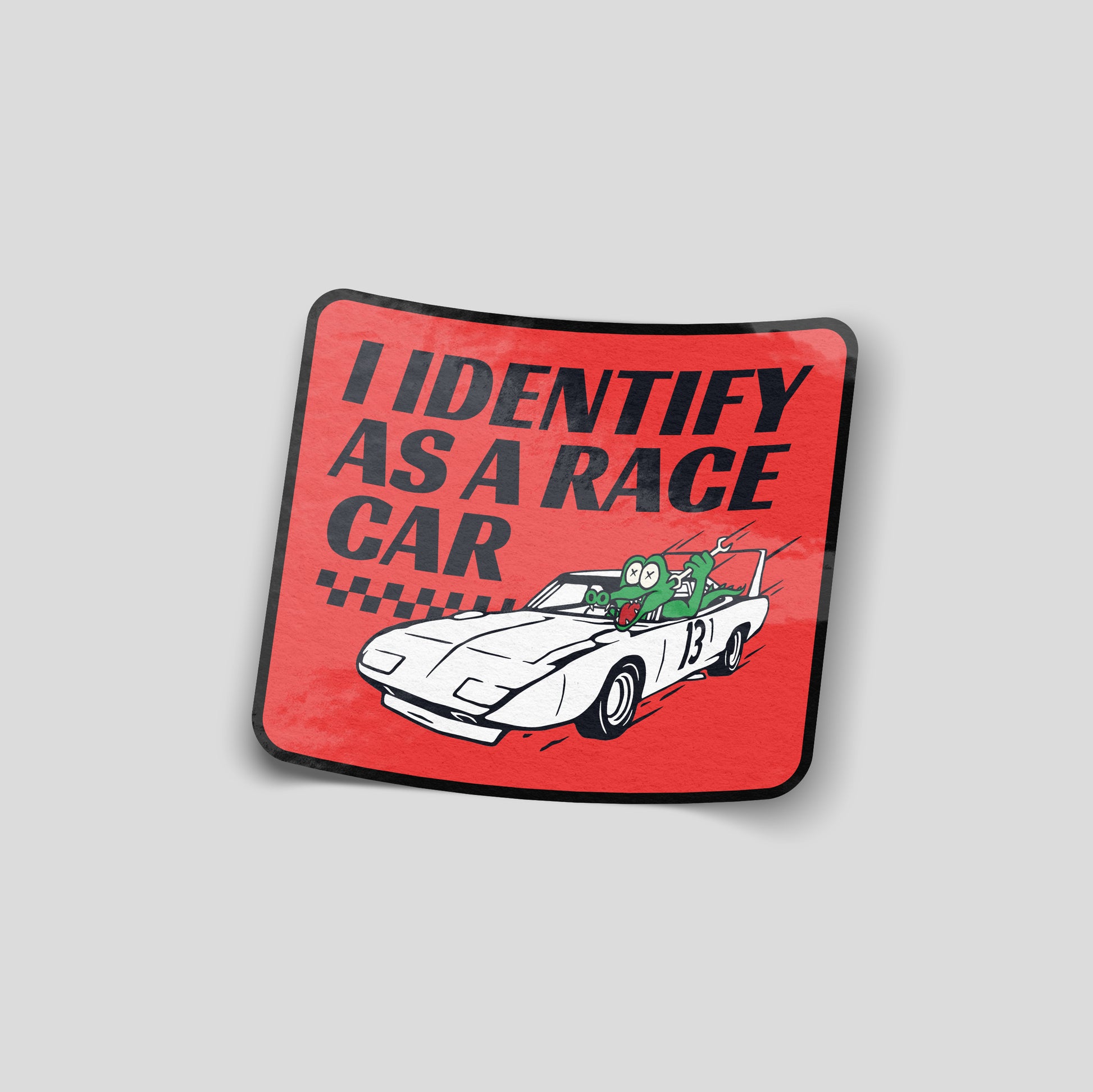 Red “I identify as a race car” funny car sticker with cartoon character driving a sports car, UK automotive humour decal.