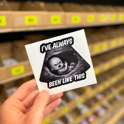 I’ve Always Been Like This funny vinyl car sticker with cheeky baby illustration, gloss laminated waterproof UK made decal held in hand by Blum Decals.