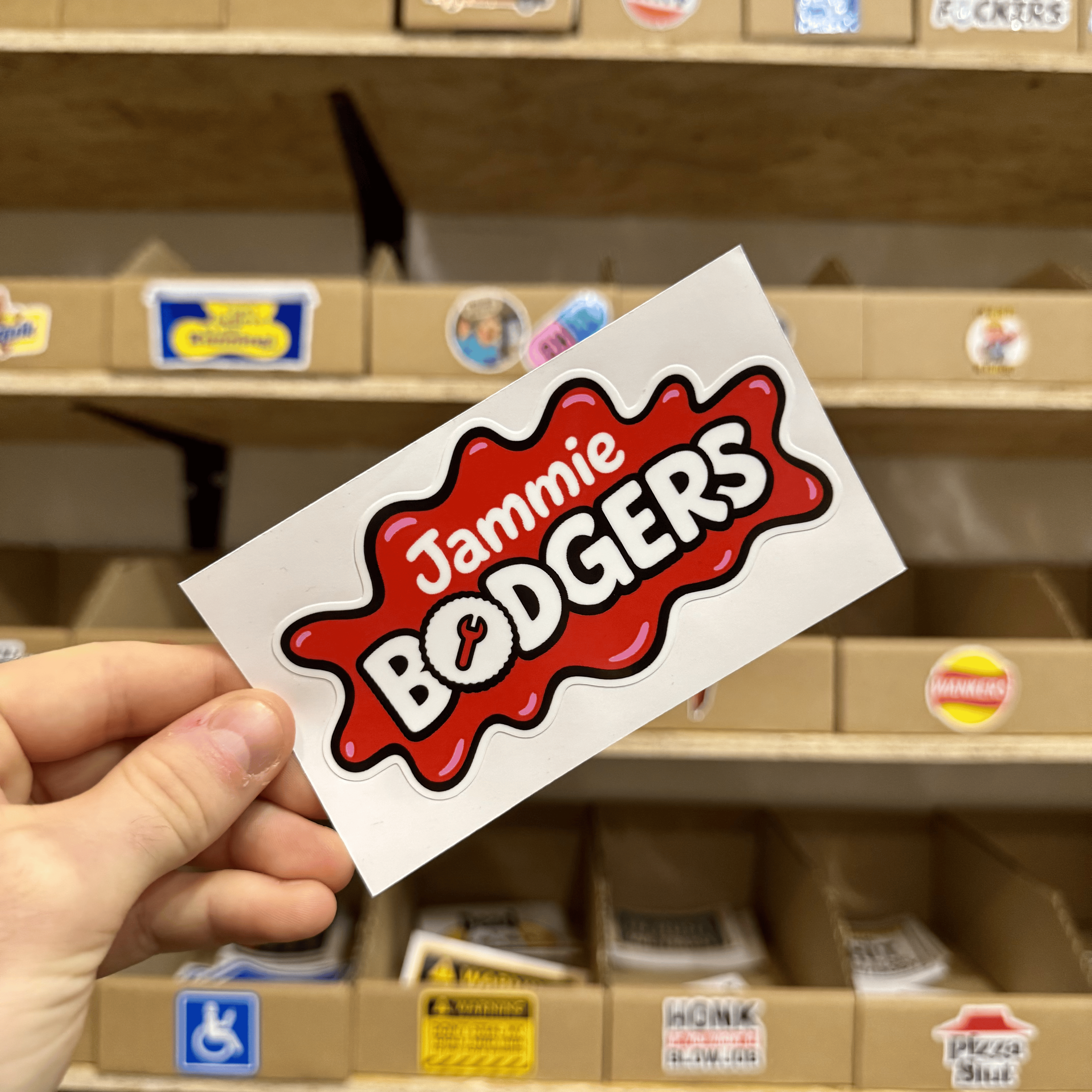 Red and white sticker resembling a splat shape with the playful text ‘Jammie Bodgers’ in bold lettering.