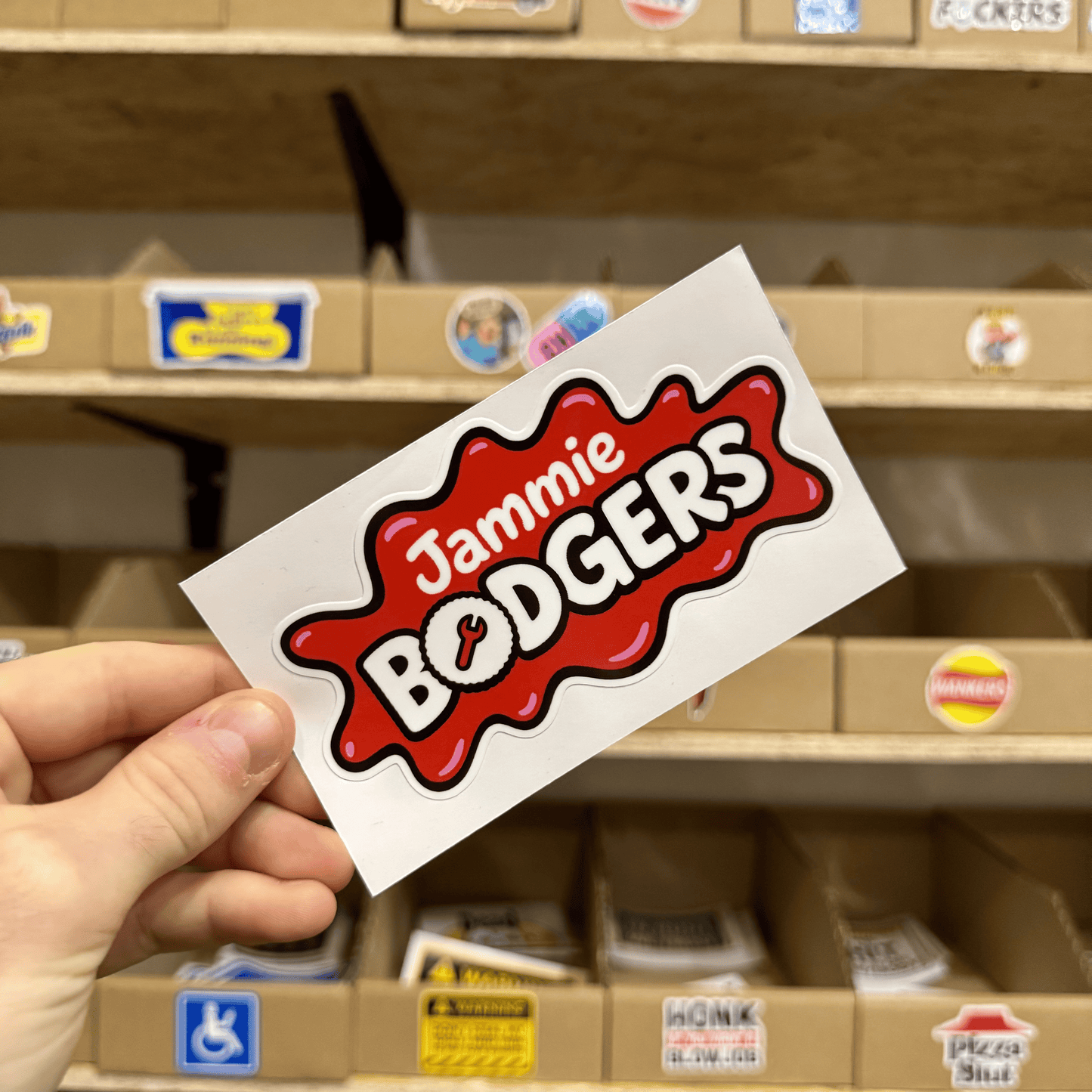 Red and white sticker resembling a splat shape with the playful text ‘Jammie Bodgers’ in bold lettering.