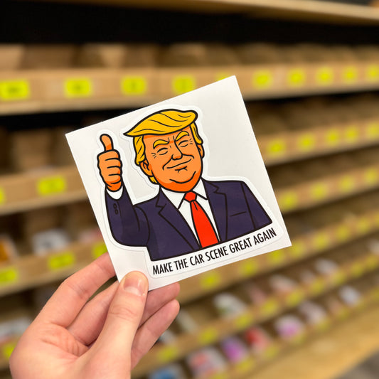 Cartoon thumbs-up character parody reading “Make the car scene great again” funny vinyl sticker held in hand.