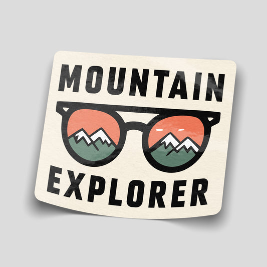 Cream Mountain Explorer sticker with black sunglasses showing green snow-capped mountains against orange skies in the lenses.