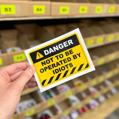 Funny hazard style sticker reading “not to be operated by idiots” yellow warning design