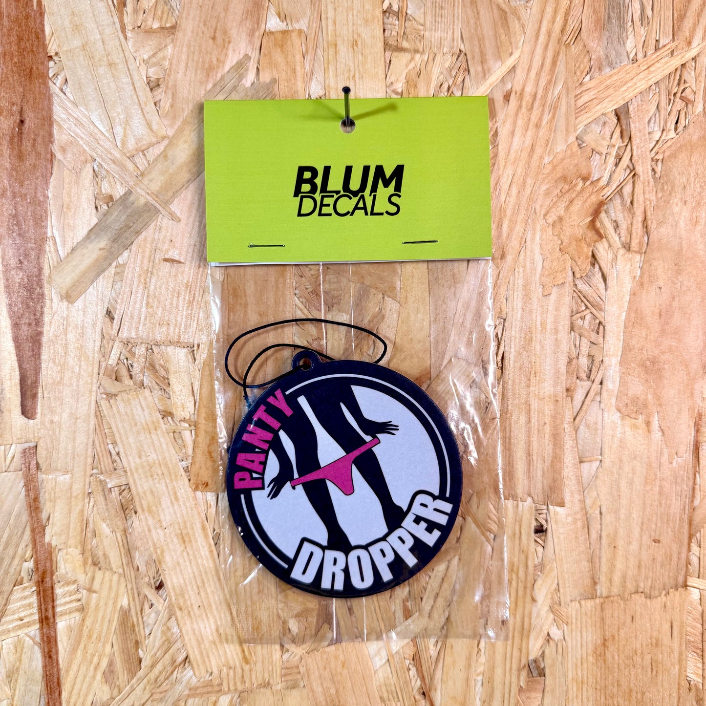 Round decal with 'Panty Dropper' design on a clear card, hanging against a wooden background.