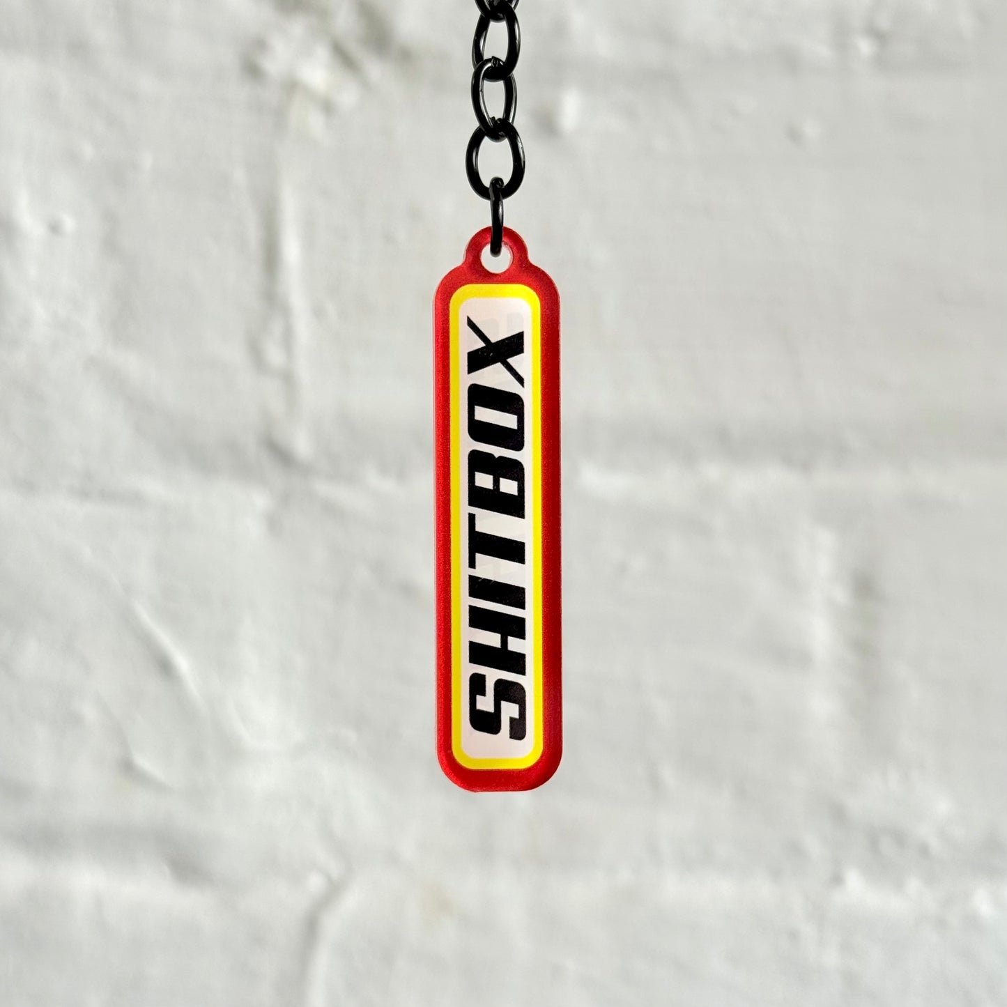 Funny “Shitbox” acrylic keychain with bold red and yellow design, glossy double-sided print and black chain, perfect for project car owners.