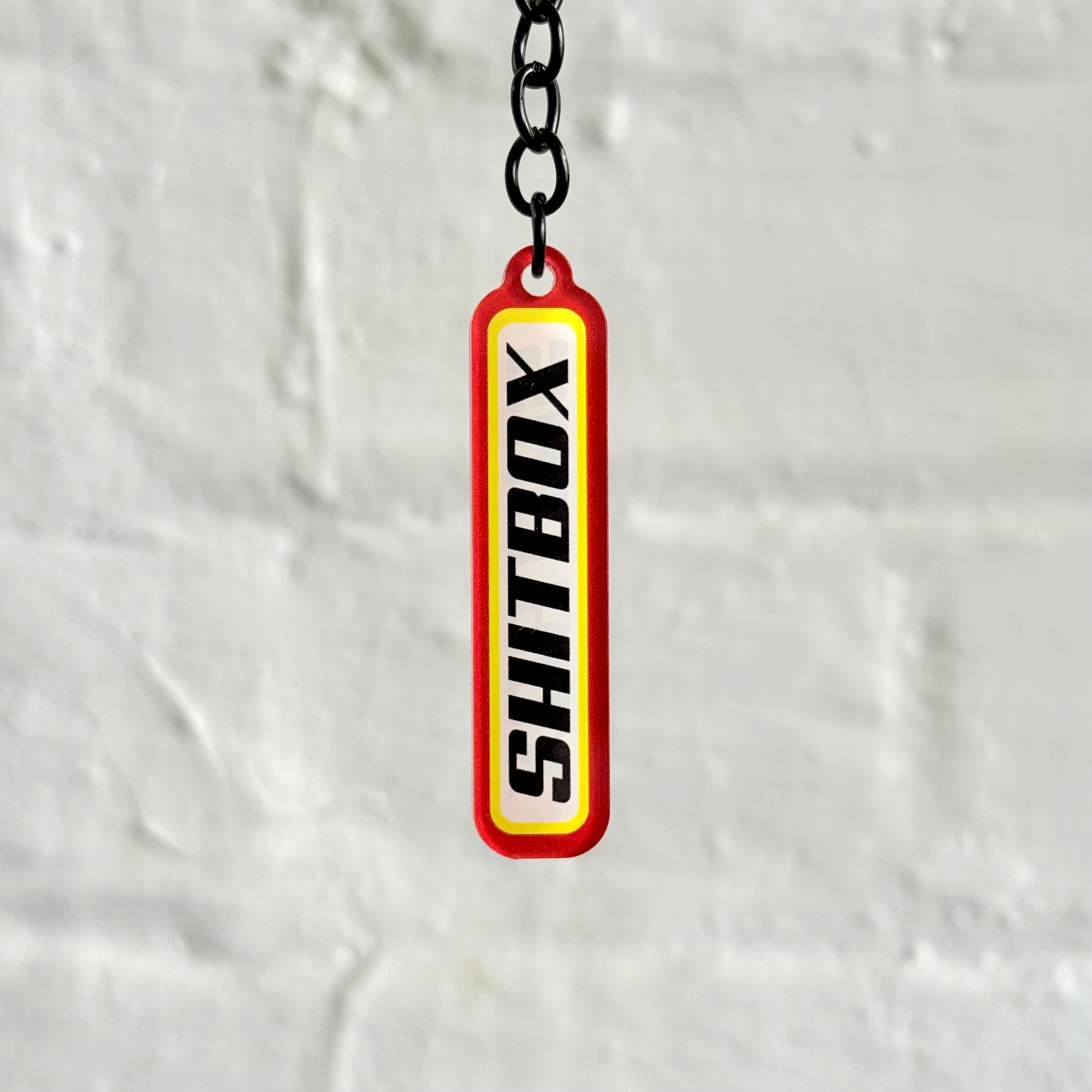 Funny “Shitbox” acrylic keychain with bold red and yellow design, glossy double-sided print and black chain, perfect for project car owners.