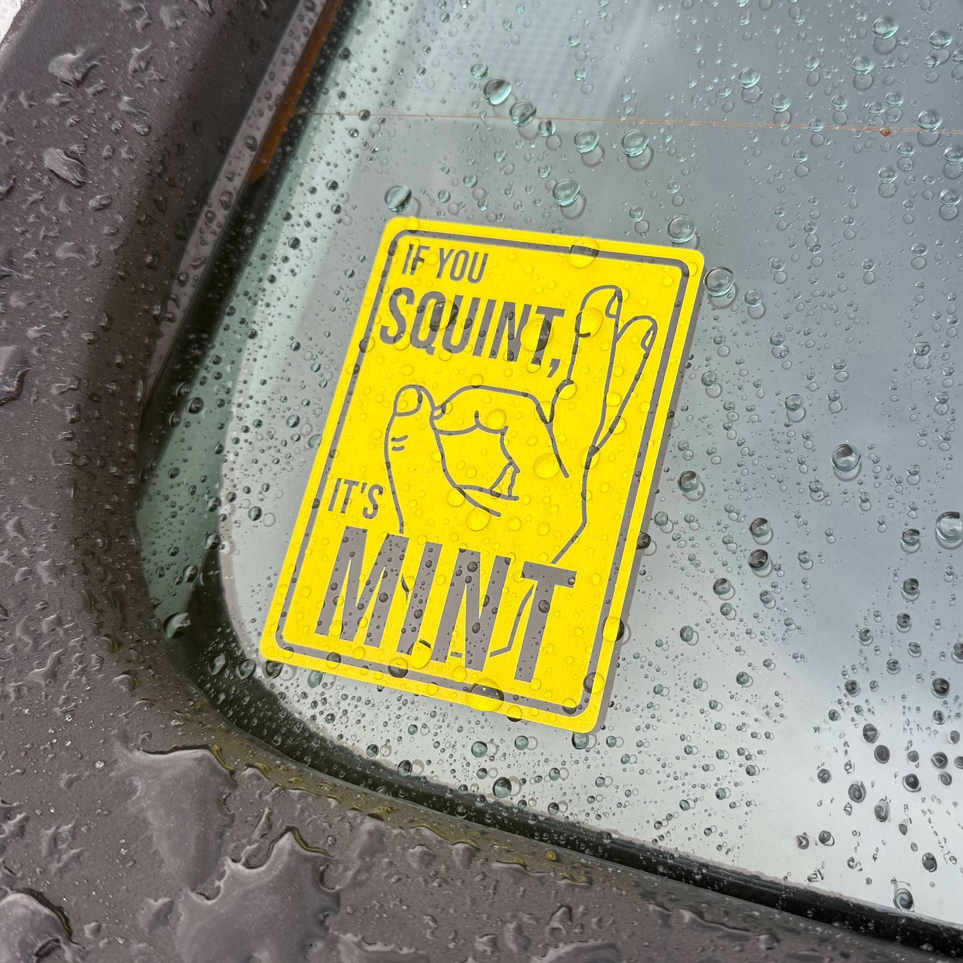 Bright yellow custom vinyl car window sticker featuring the playful “If You Squint, It’s Mint” slogan and hand gesture illustration, showcasing creative sticker design and vehicle graphics.