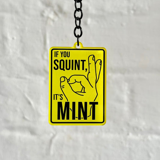 Funny “If You Squint It’s Mint” acrylic keychain with yellow sign-style design, glossy finish and black chain, ideal car enthusiast gift.