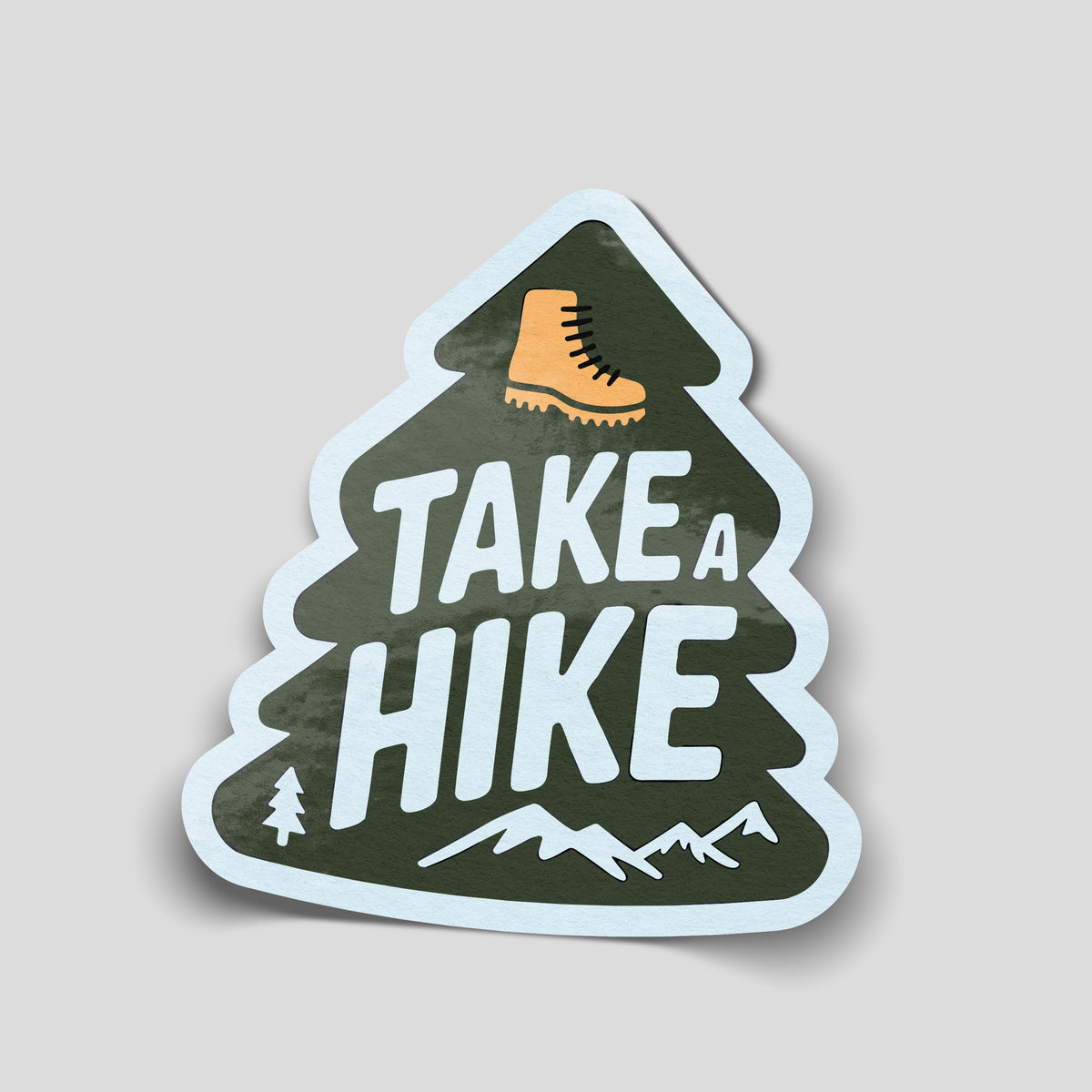 Dark green pine tree-shaped Take A Hike sticker with white lettering, an orange walking boot and white mountain illustrations.