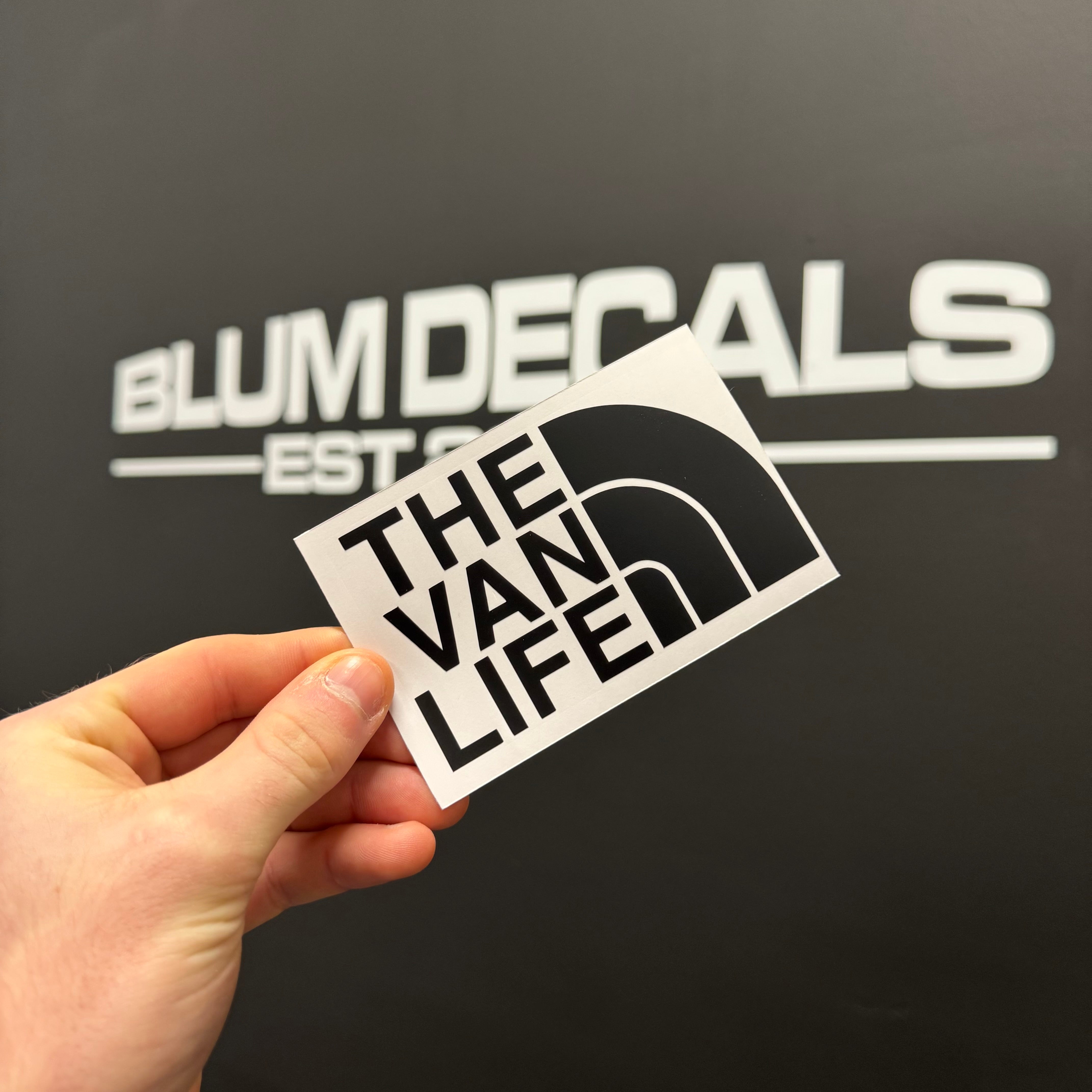 Black and white 'The Van Life' vinyl decal sticker inspired by outdoor adventure, held against a dark background with Blum Decals branding in the background.