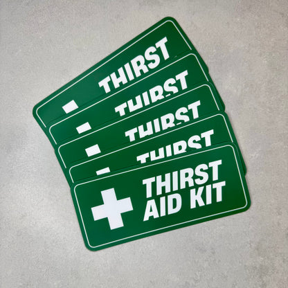 Thirst Aid Kit funny magnet stack shown on grey surface featuring green first aid style design. Removable novelty fridge or toolbox magnet with matte laminate finish made using 0.8mm magnetic sheet by Blum Decals UK.