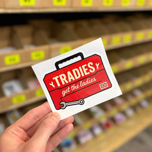 Red toolbox design reading “Tradies get the ladies” funny vinyl sticker held in hand.