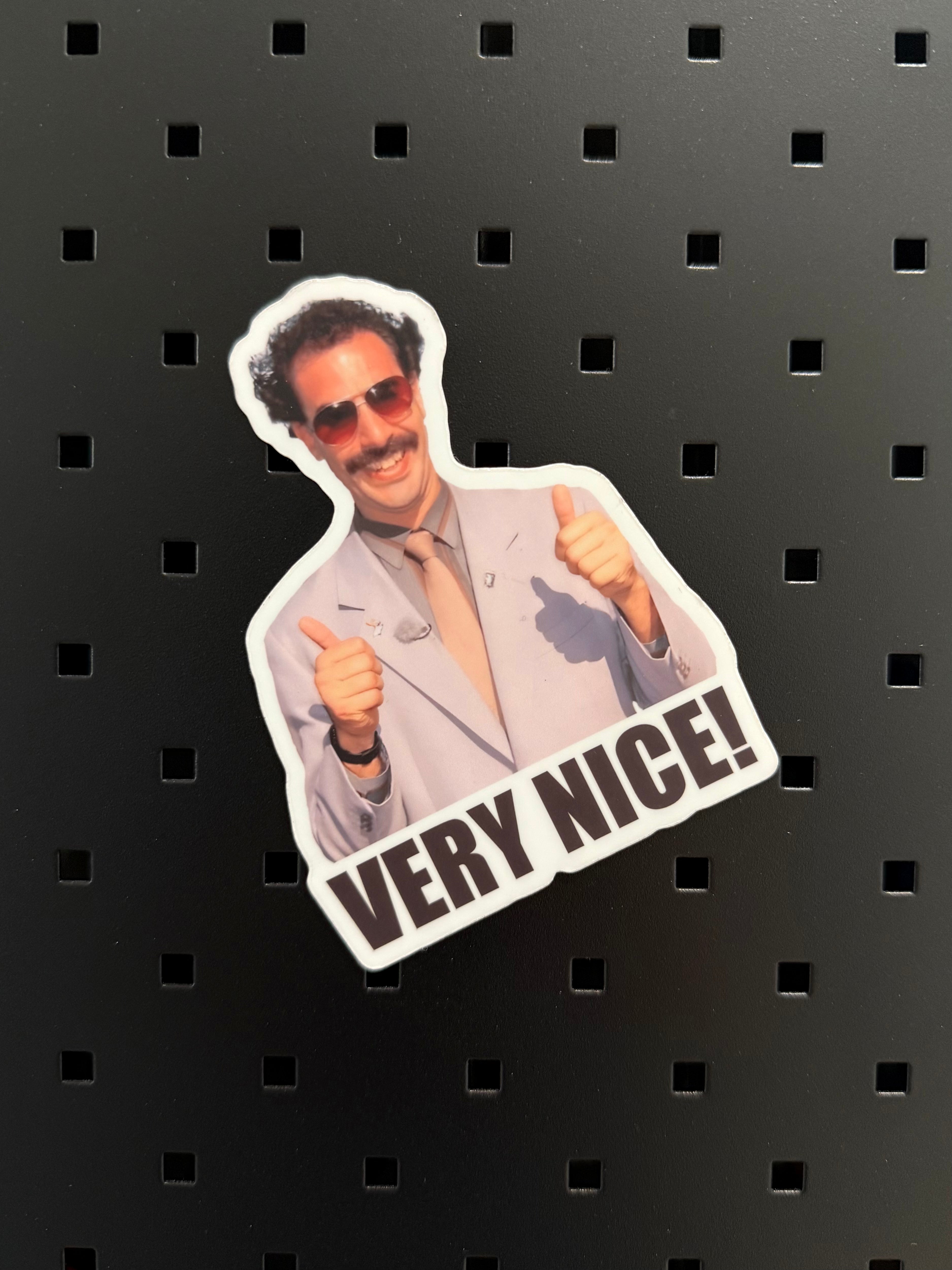 “Very Nice!” funny sticker featuring a thumbs-up character in sunglasses, displayed on a black pegboard background.