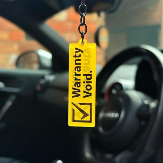 Yellow “Warranty Void” funny acrylic keychain hanging inside car with gloss black chain and heavy-duty keyring loop